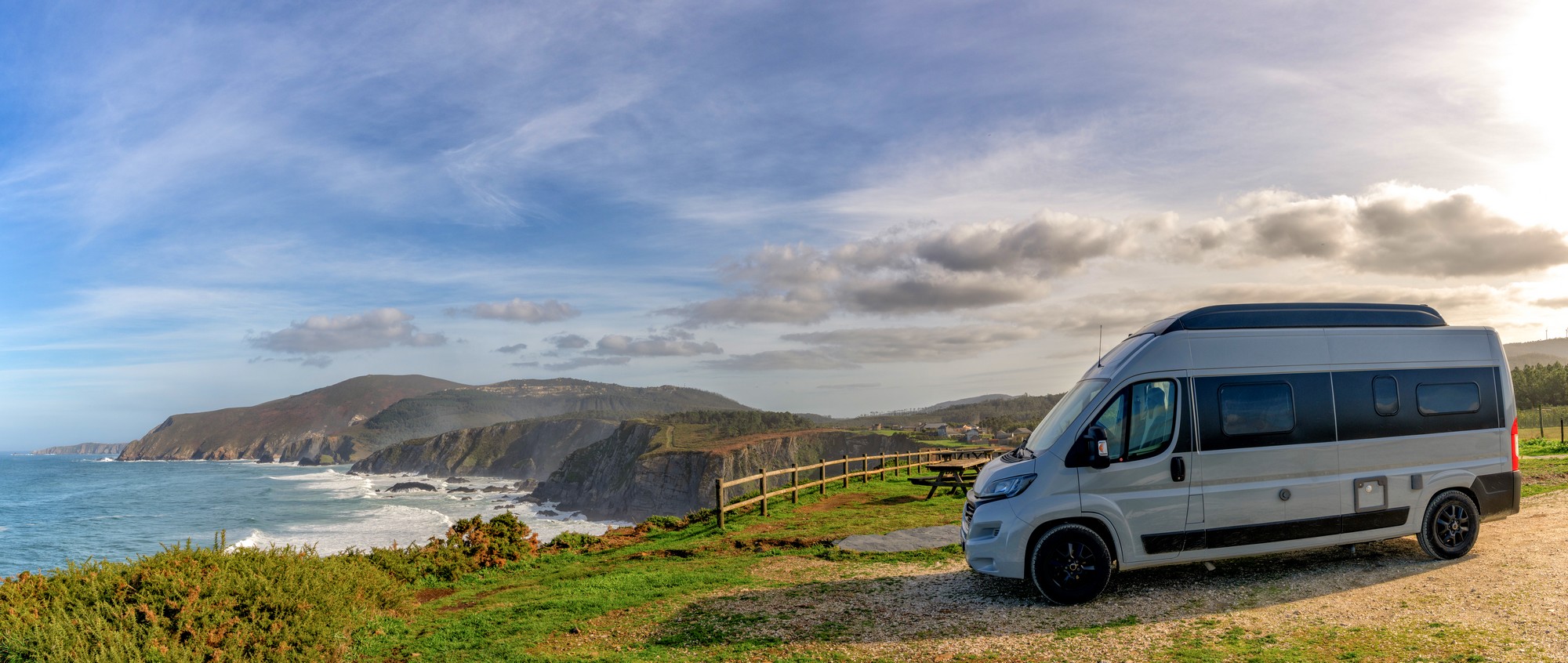 Panorama of a camper van parked high up on cliffs of a wild and rugged coastline
