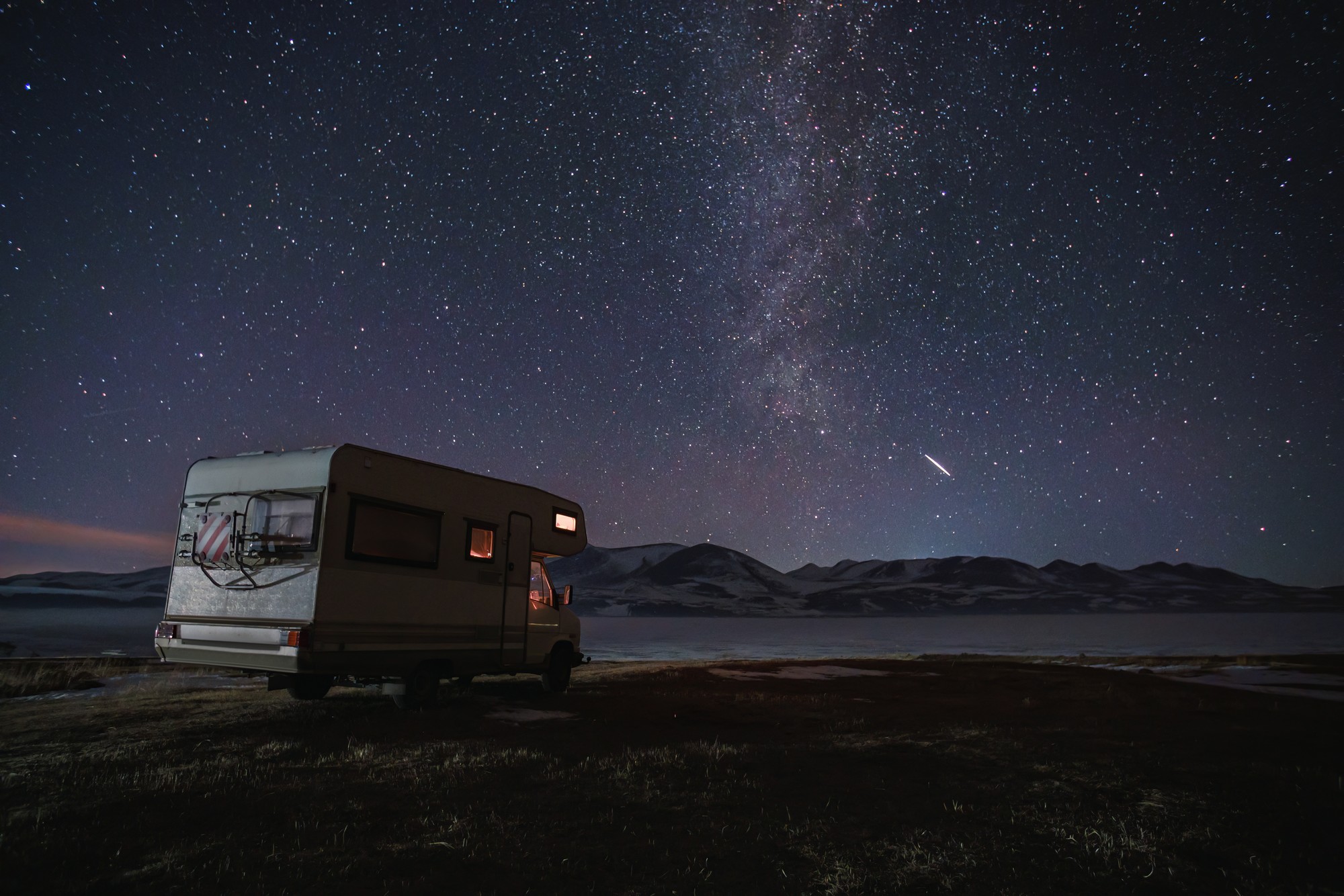 motor home under the starry sky against the backdrop of the mountains in winter